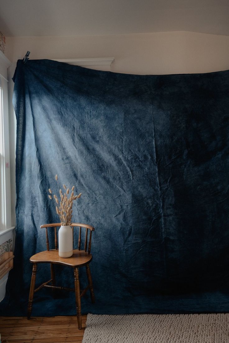 a chair sitting in front of a blue backdrop with a vase on top of it