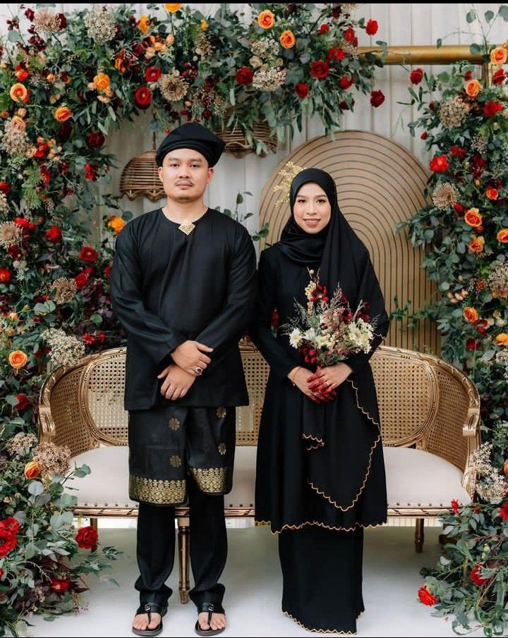 a man and woman standing next to each other in front of a floral arch with flowers