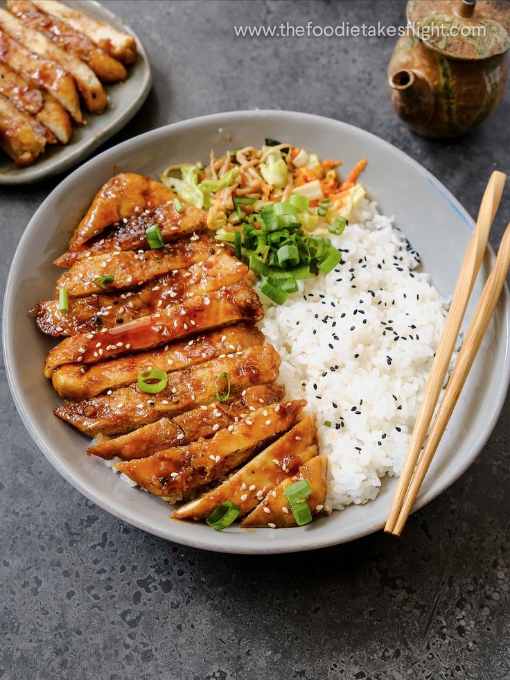 a plate with chicken, rice and chopsticks on it