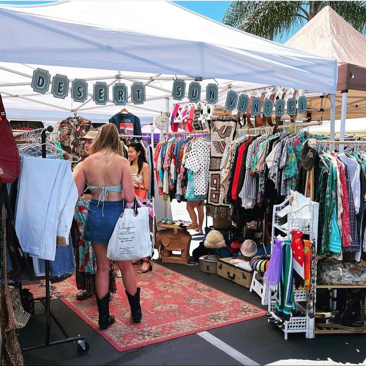 a woman is looking at clothes on display in a market stall under a white tent