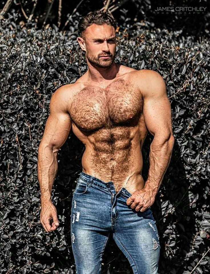 a shirtless man standing in front of bushes