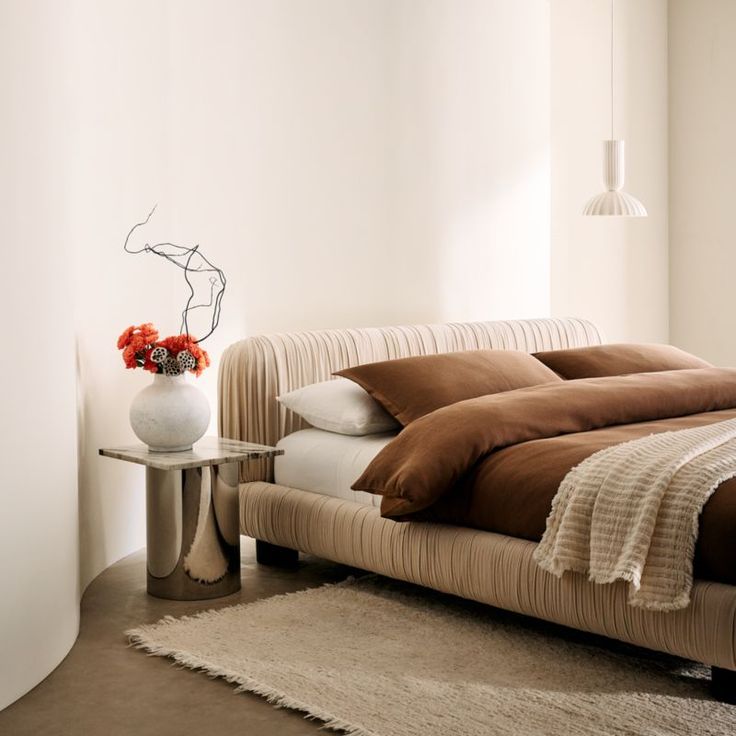 a bed with brown and white comforters in a bedroom next to a vase filled with flowers