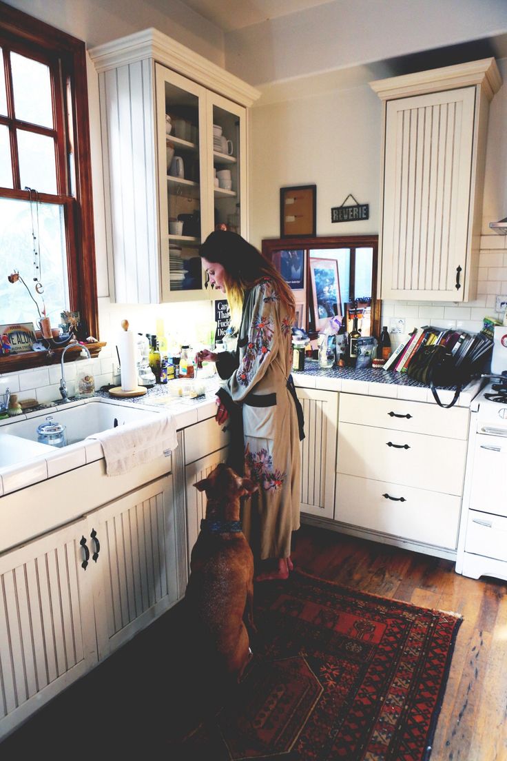 a woman standing in a kitchen next to a dog looking at something on the counter