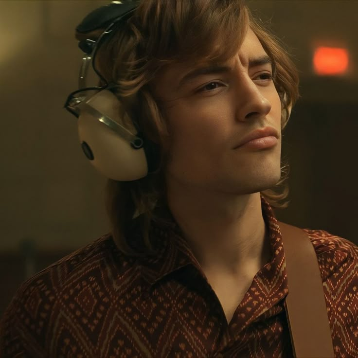 a young man with headphones on his ears looking off to the side in a dimly lit room