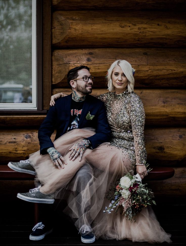 a man and woman sitting next to each other in front of a log cabin wall