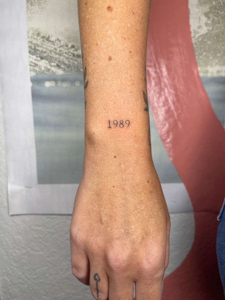 a person with a small tattoo on their left wrist and the word 1989 written in black ink