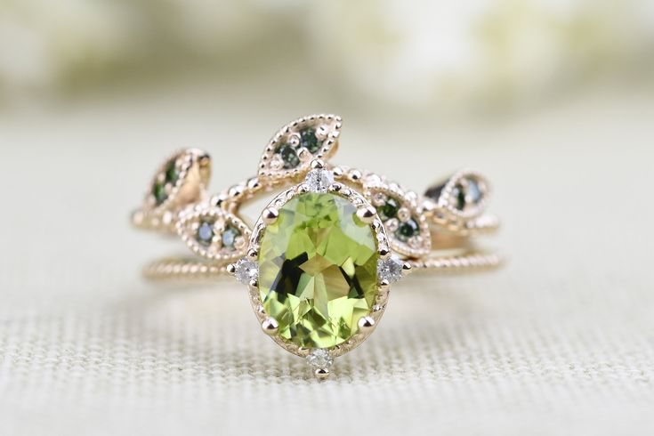 a ring with an oval shaped green stone surrounded by leaves and diamonds on a white surface