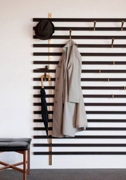 a coat rack with clothes hanging on it next to a chair and wall mounted coat rack