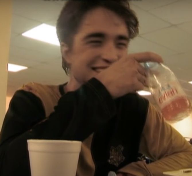 a man sitting at a table drinking from a plastic cup with his hand on his face