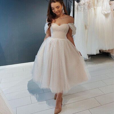 a woman in a white dress is looking down at her wedding gowns on display