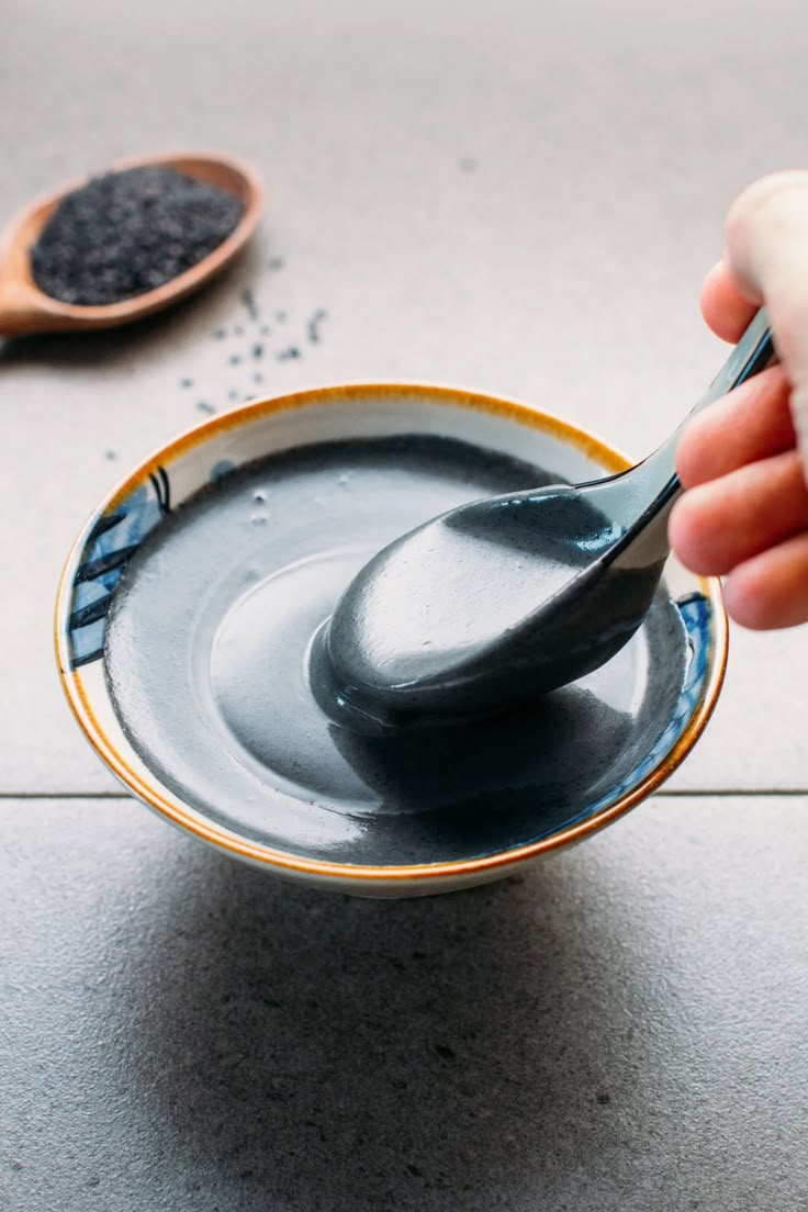 a hand holding a spoon over a bowl filled with black liquid