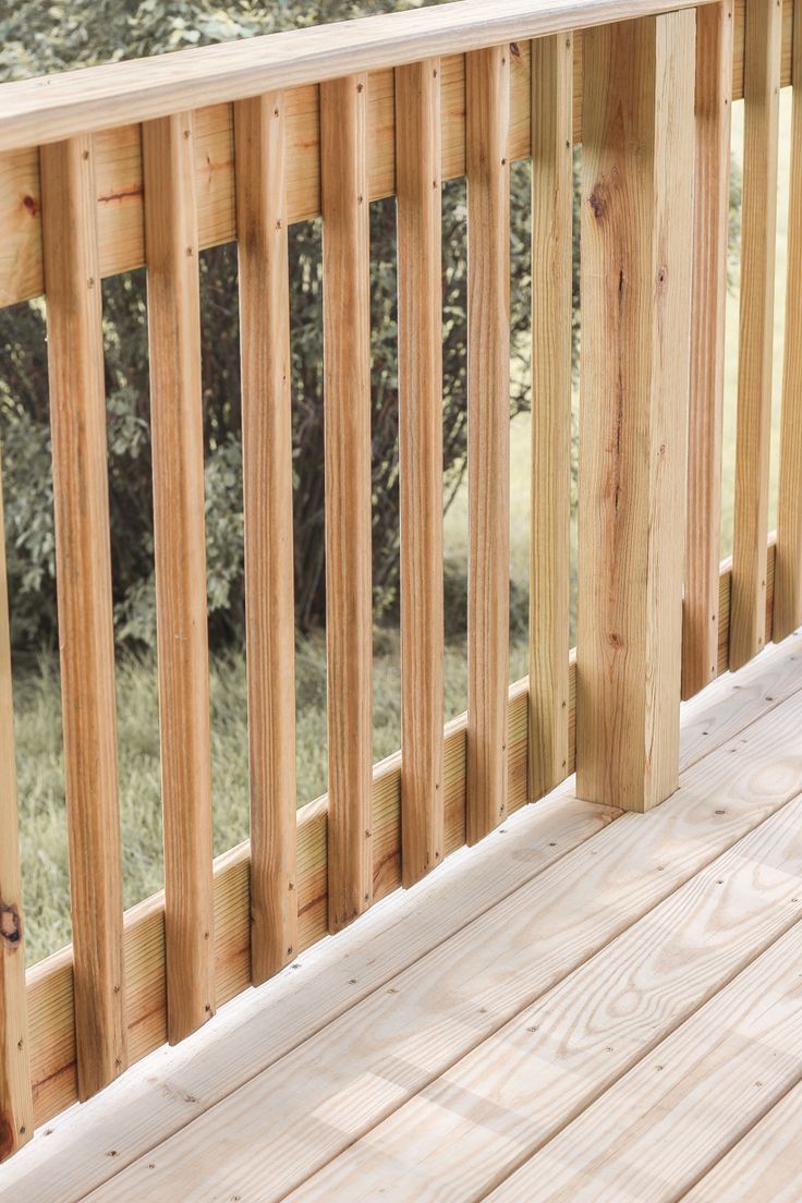 a wooden deck with railings and trees in the background