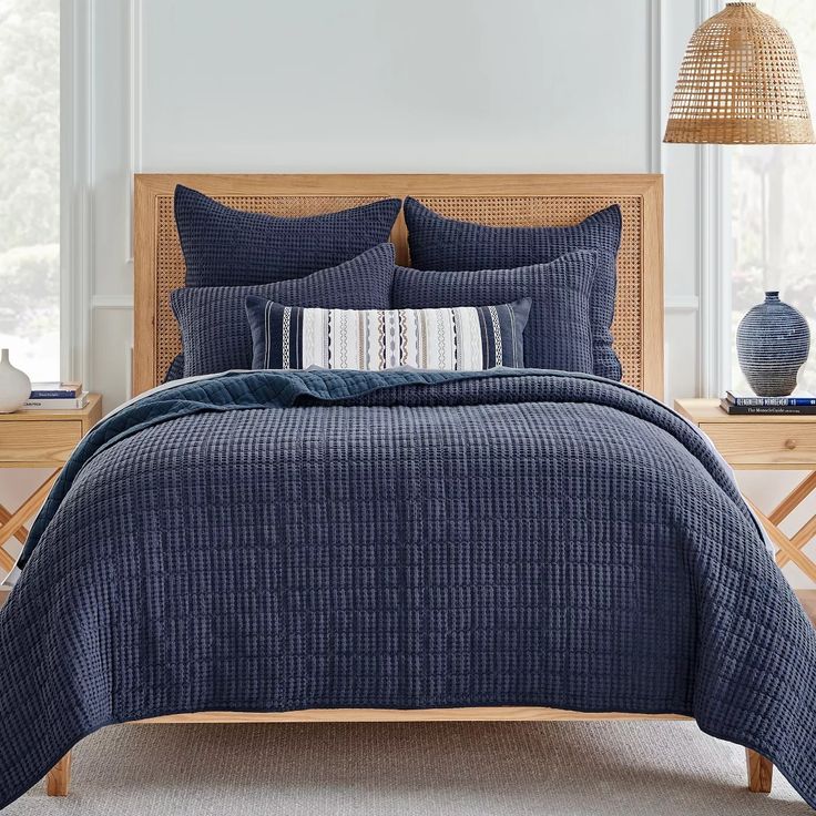 a bed with blue bedspread and pillows in a white room next to a window