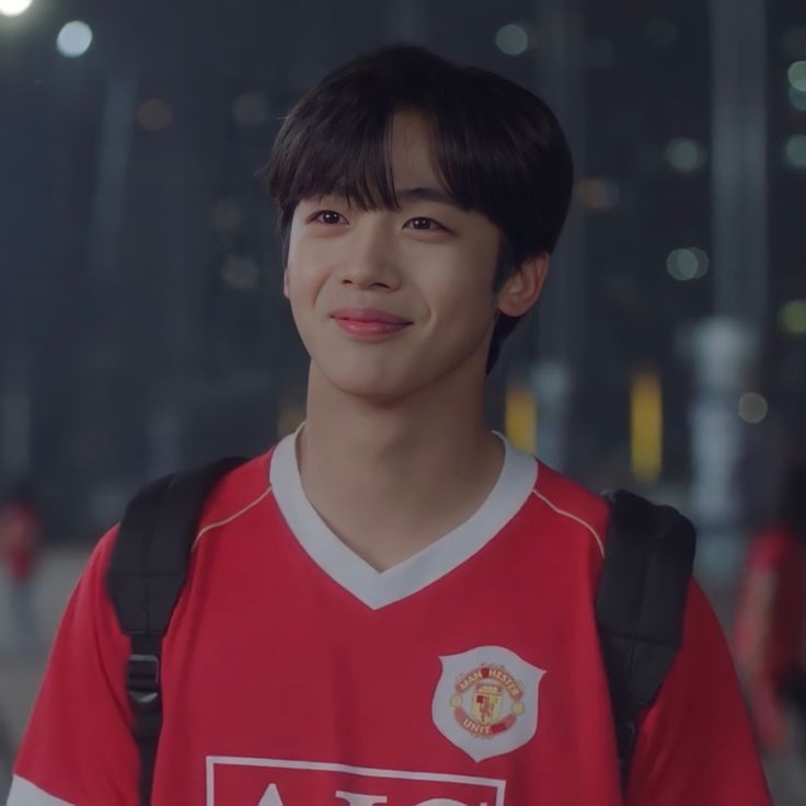 a young man wearing a red and white shirt standing in front of a building at night