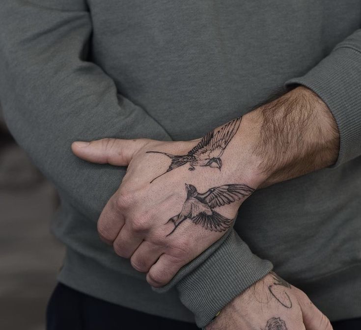 a man's hand with two birds tattooed on his left wrist and the other arm