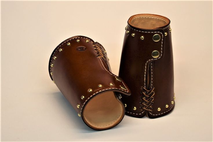 two brown leather cups sitting next to each other on top of a white surface with gold rivets