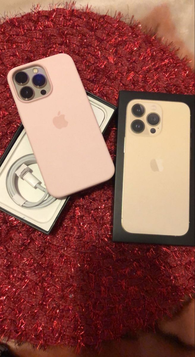 two iphones sitting on top of a red carpet next to each other, one is pink and the other is white