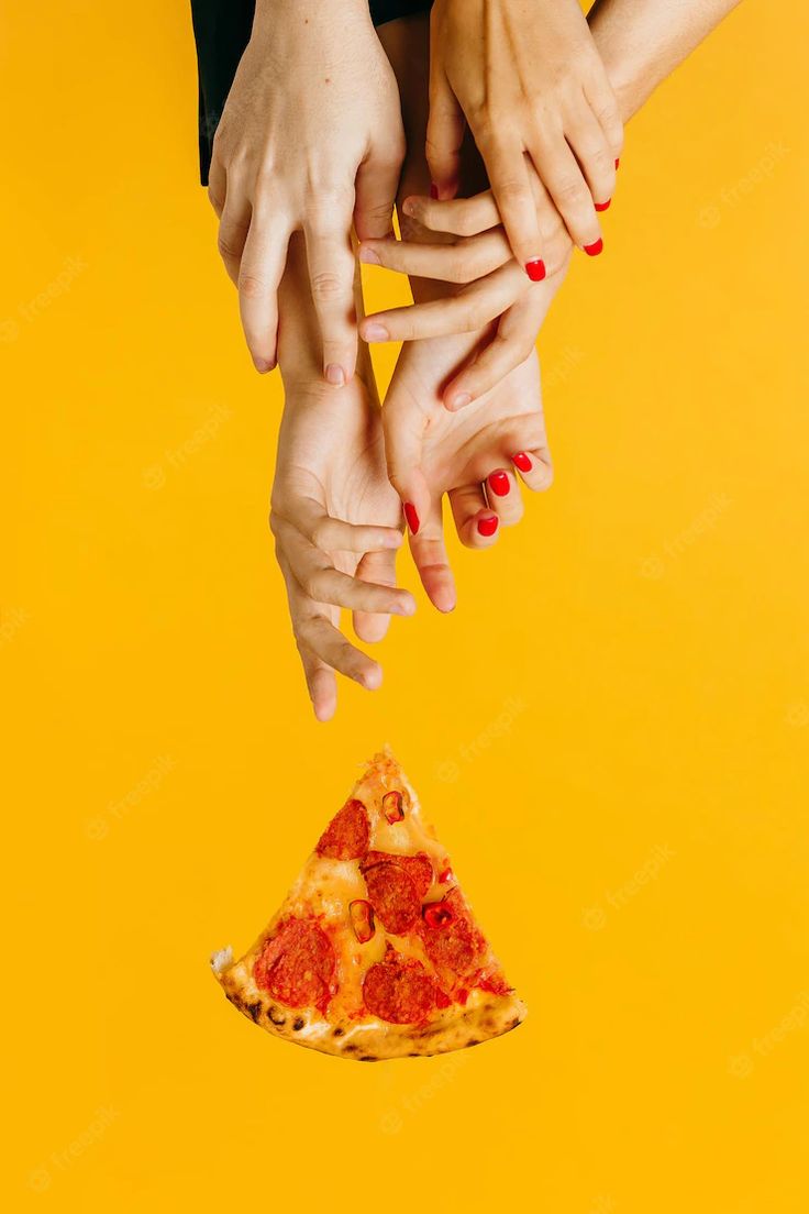 two hands reaching for a slice of pizza on a yellow background with red nail polish