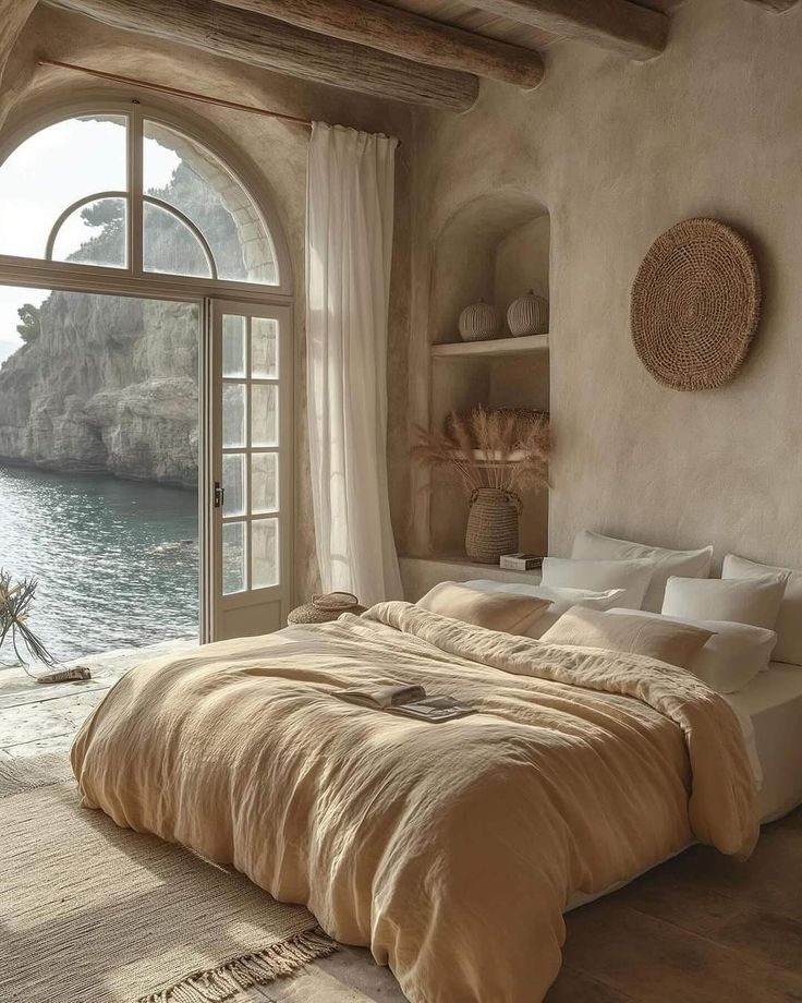 a large bed sitting next to an open window in a bedroom near the ocean and mountains