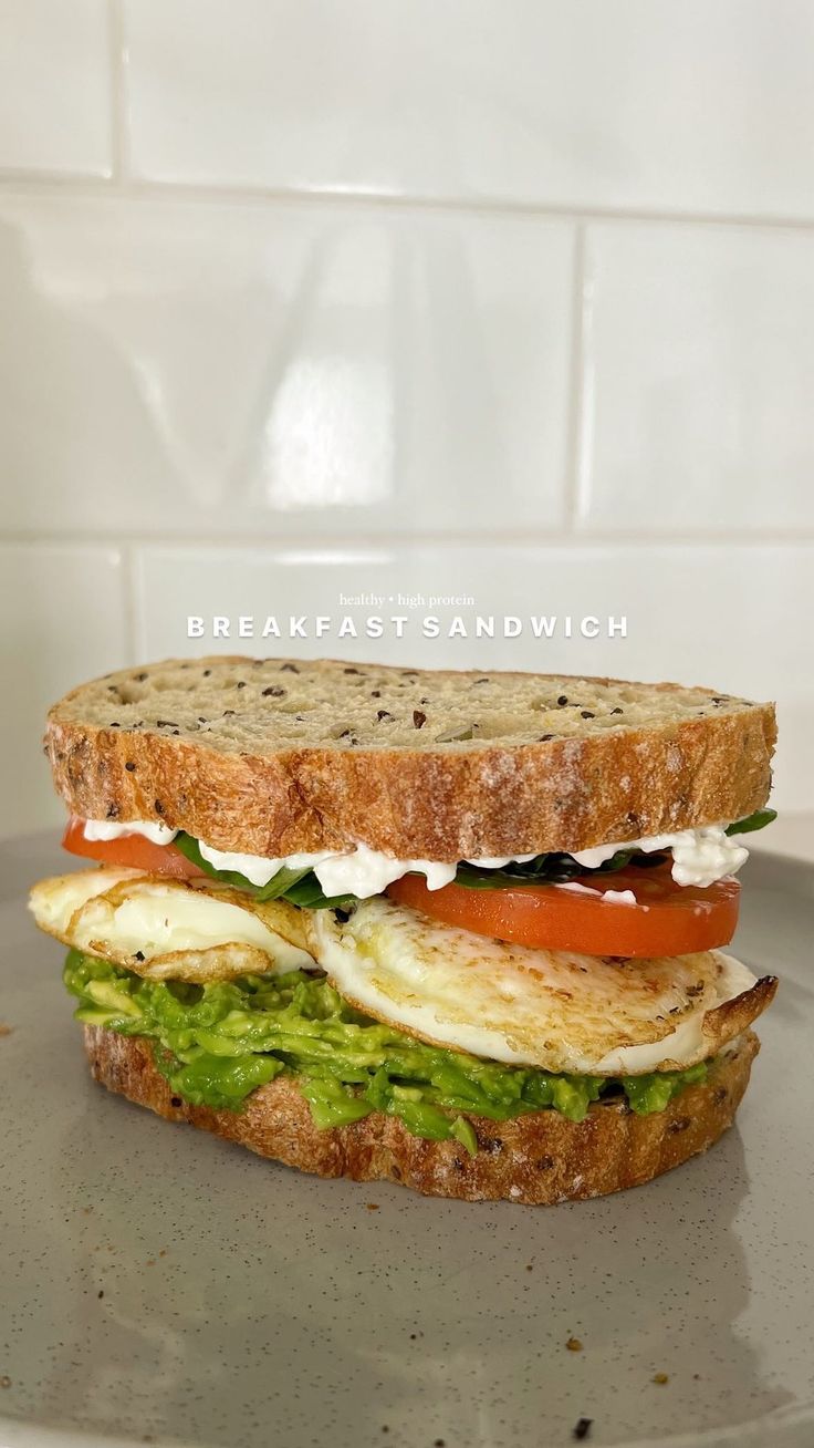 a sandwich with egg, tomato and avocado on toasted bread sitting on a plate