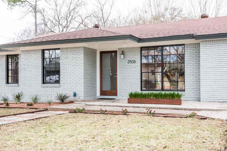 a white brick house with a brown door and window panes on the front porch