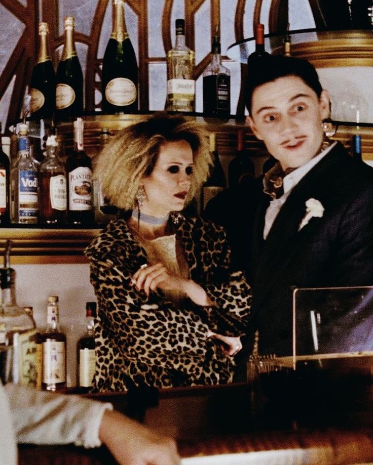 a man standing next to a woman in front of a bar filled with liquor bottles