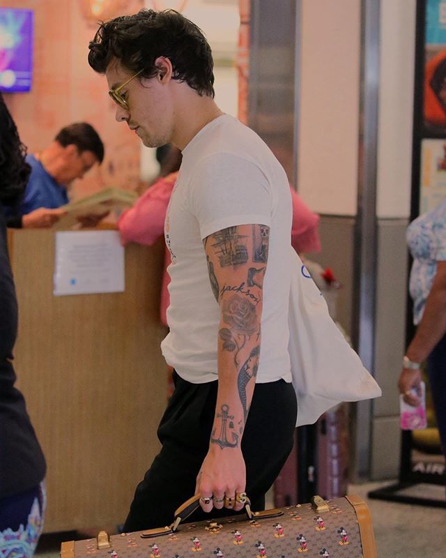 a man carrying a suitcase with tattoos on his arm and shoulder, in an airport