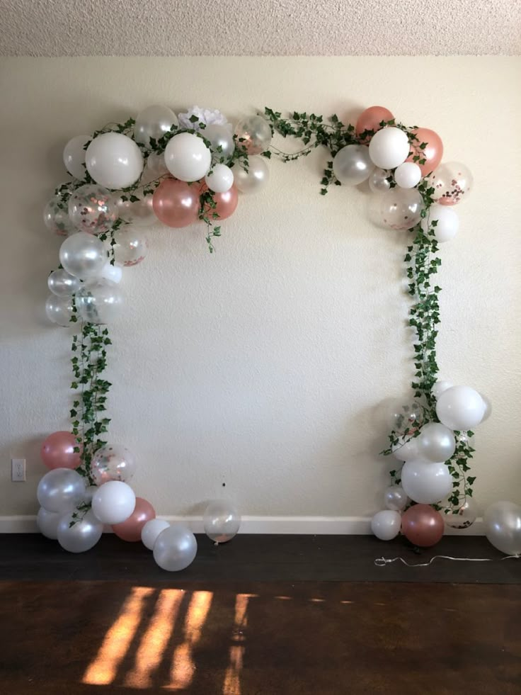 an arch made out of balloons and greenery is displayed on the wall in this room