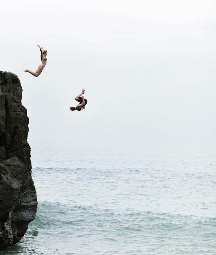 two people jumping off rocks into the ocean from a cliff near some water and one person is in mid air