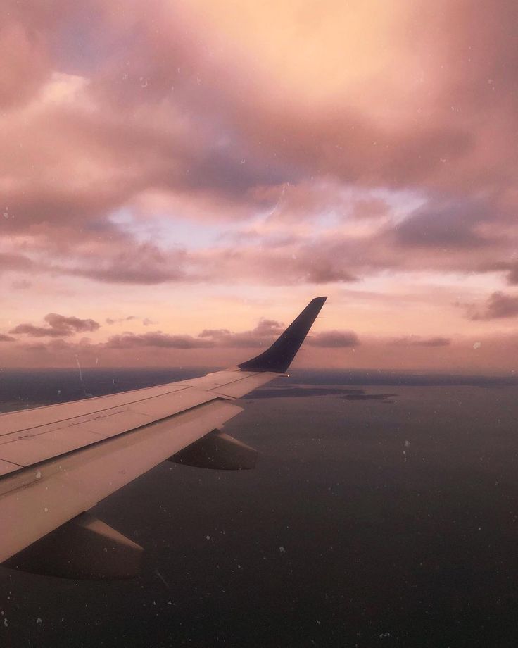 the wing of an airplane as it flies in the sky with clouds and water below