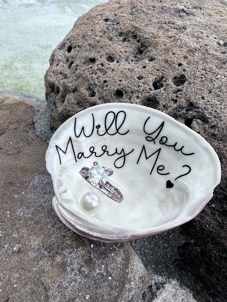 a ring dish with writing on it sitting on top of a rock next to the ocean