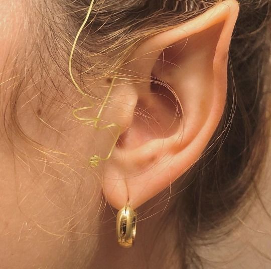 a close up of a person's ear wearing gold earrings