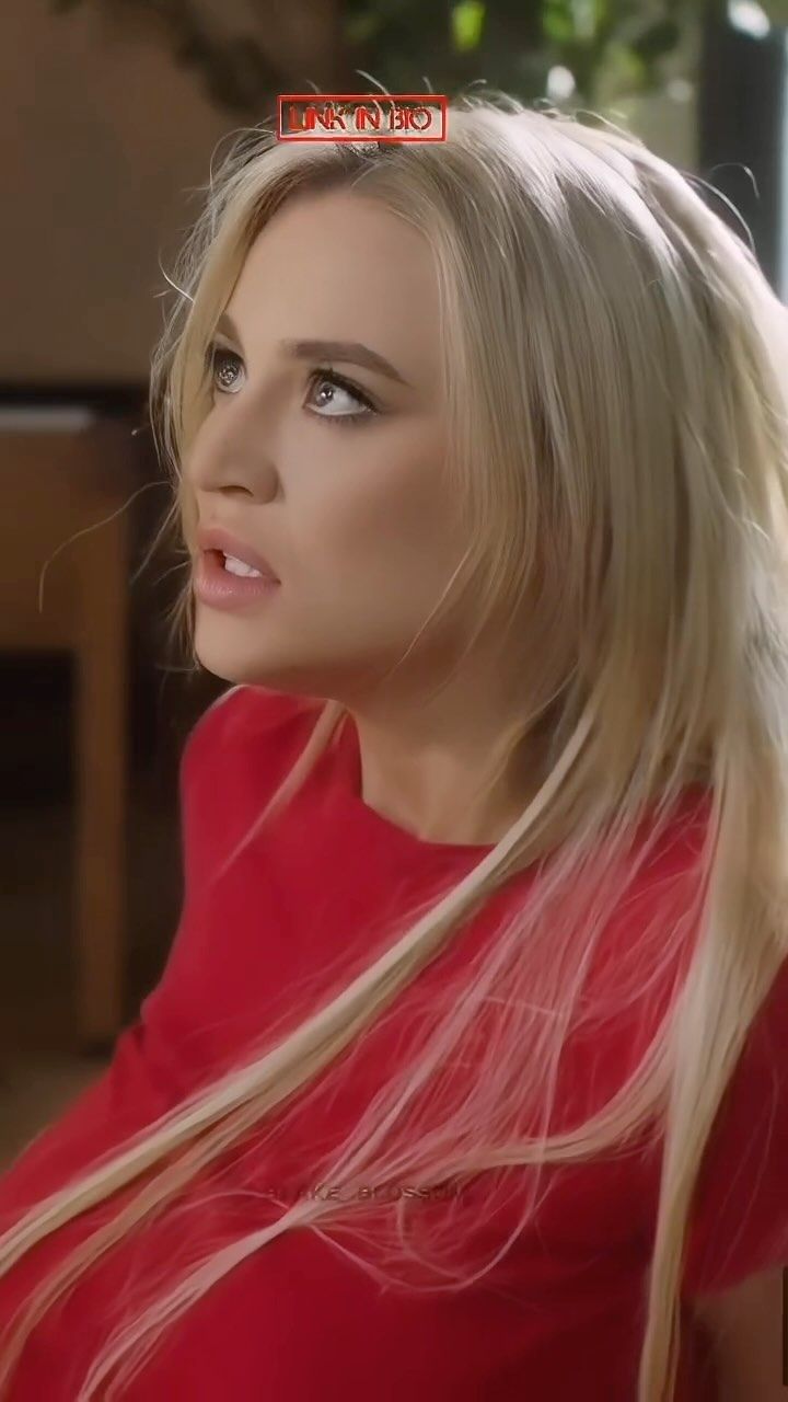 a woman with long blonde hair wearing a red shirt and looking off to the side