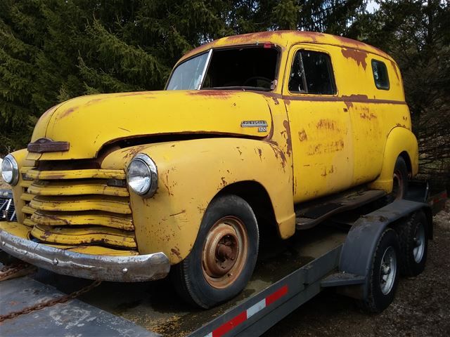 an old yellow truck sitting on top of a flatbed trailer in front of some trees