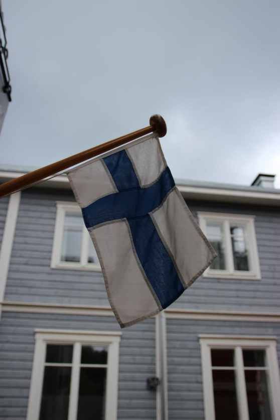 a blue and white flag on a pole in front of a gray house with windows