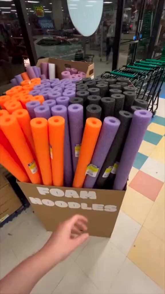 a cardboard box filled with purple and orange crepe rods in a store aisle