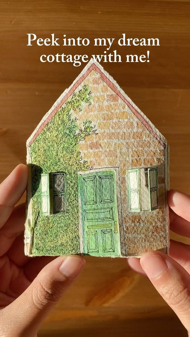 someone is holding up a small paper house with the words peek into my dream cottage with me