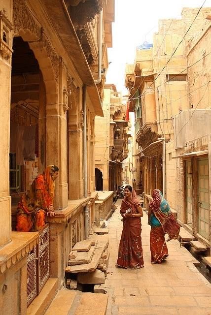 two women in sari walking down an alley way with stone buildings on either side