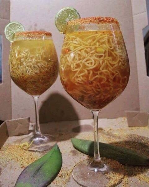 two glasses filled with noodles and vegetables on a table next to an avocado