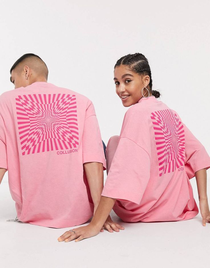 a man and woman sitting on the ground wearing matching pink t - shirts with an abstract design