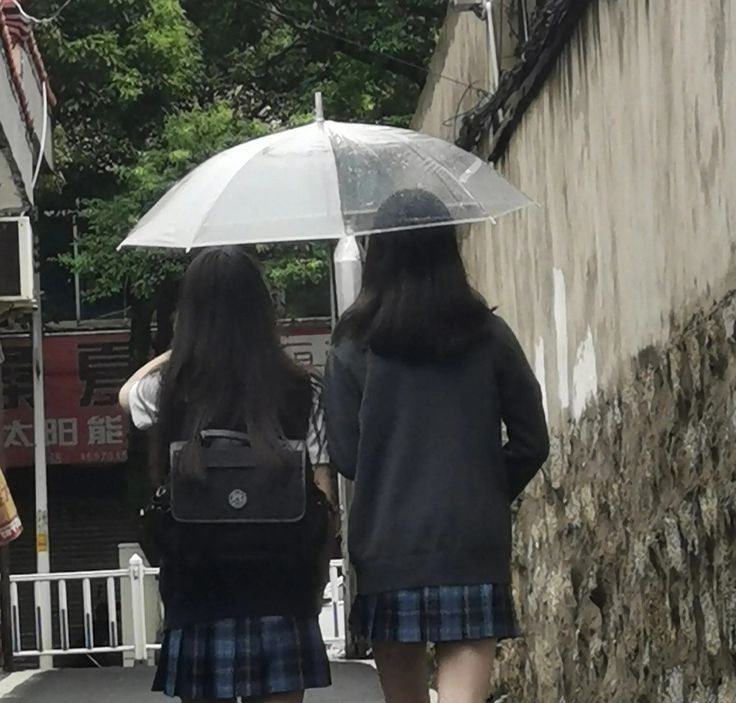 two girls walking down the street with an umbrella over their heads and one holding a backpack