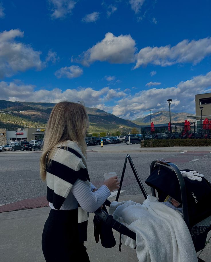 a woman standing next to a baby in a stroller on the side of the road