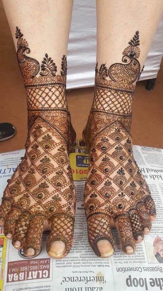 two feet with henna tattoos on top of each other and one foot has an intricate design