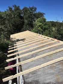 an unfinished roof is being installed on a house in the woods with trees and bushes behind it