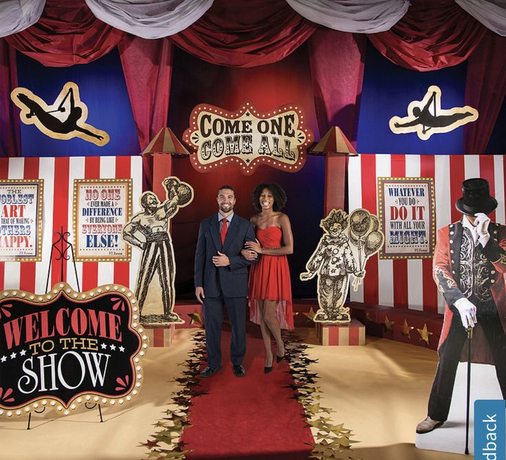 a man and woman are standing on a red carpet in front of some circus booths