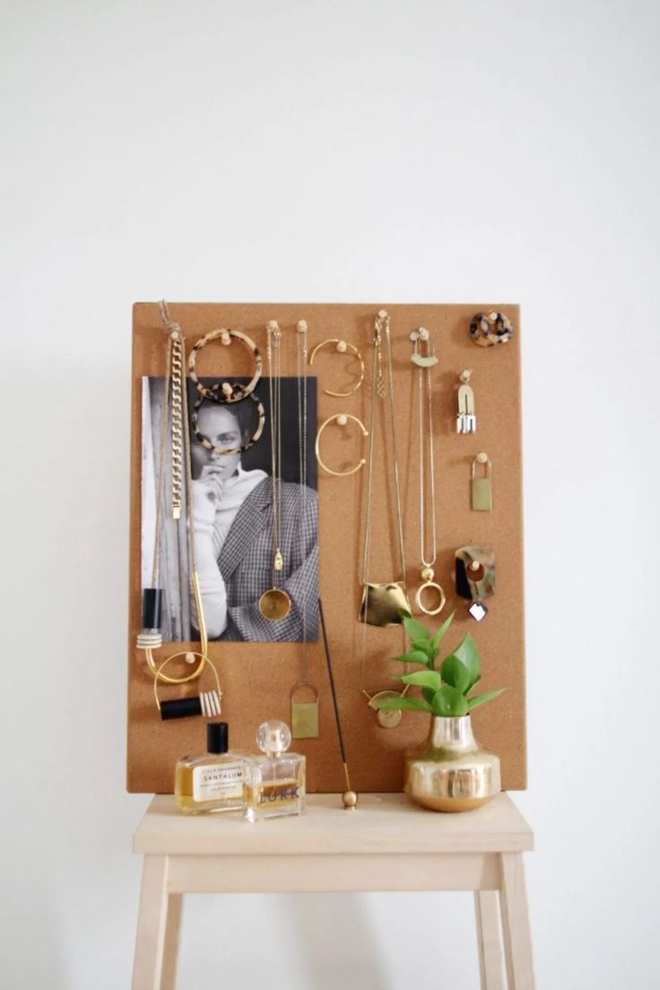 a wooden table topped with lots of jewelry next to a wall mounted photo on a cork board