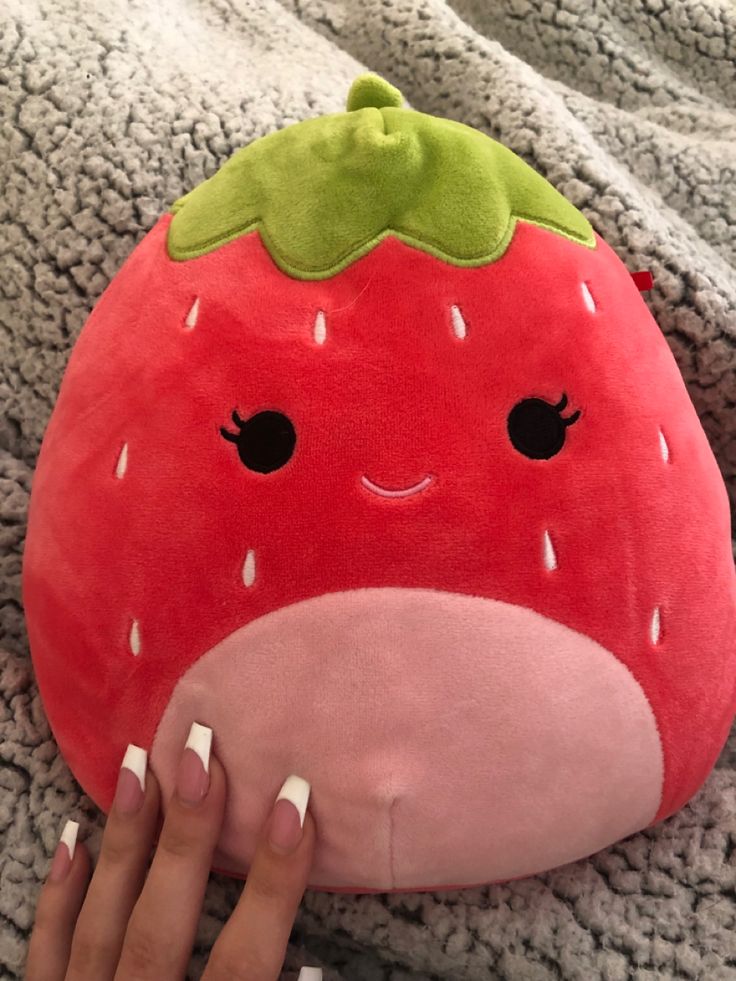 a person is holding a strawberry pillow on the ground with their hand and fingers resting on it