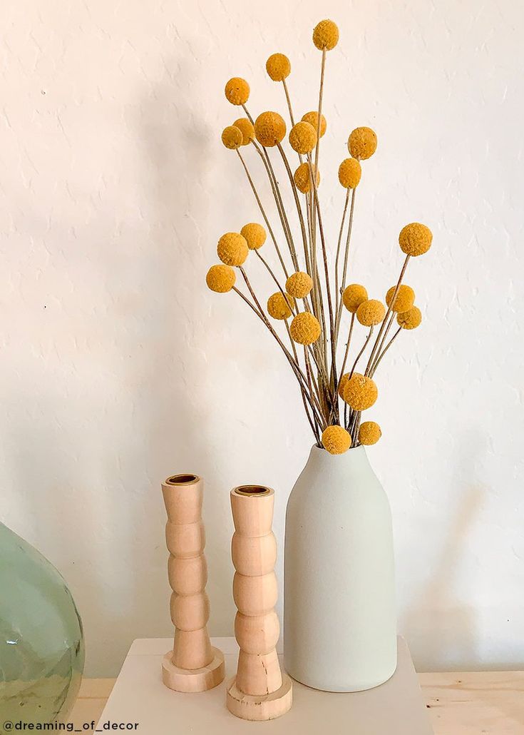 two vases with yellow flowers in them on a white shelf next to a glass vase