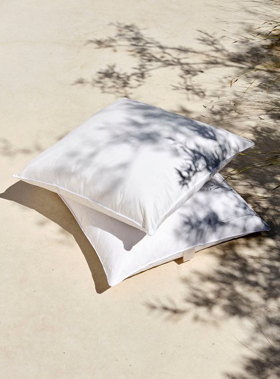 two white pillows sitting on top of each other next to a tree branch in the shade