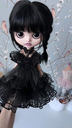 a doll is wearing a black dress and holding her hand up in front of the camera